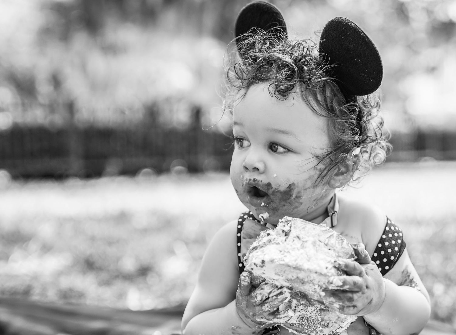 black and white photo of a baby looking away holding a cake with cake on his face