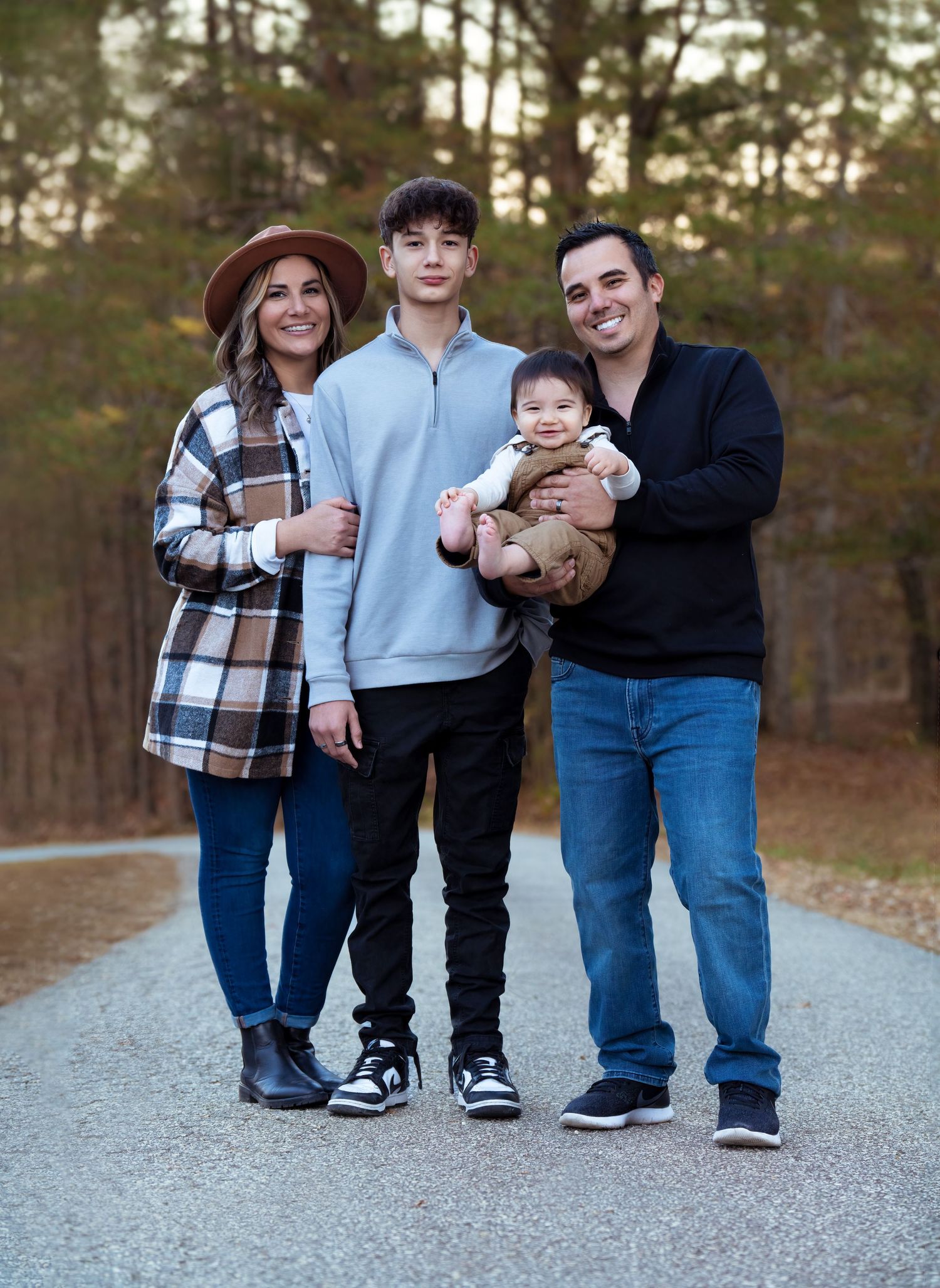 Family photo outdoors of a family standing on a concrete driveway with foliage in the background
