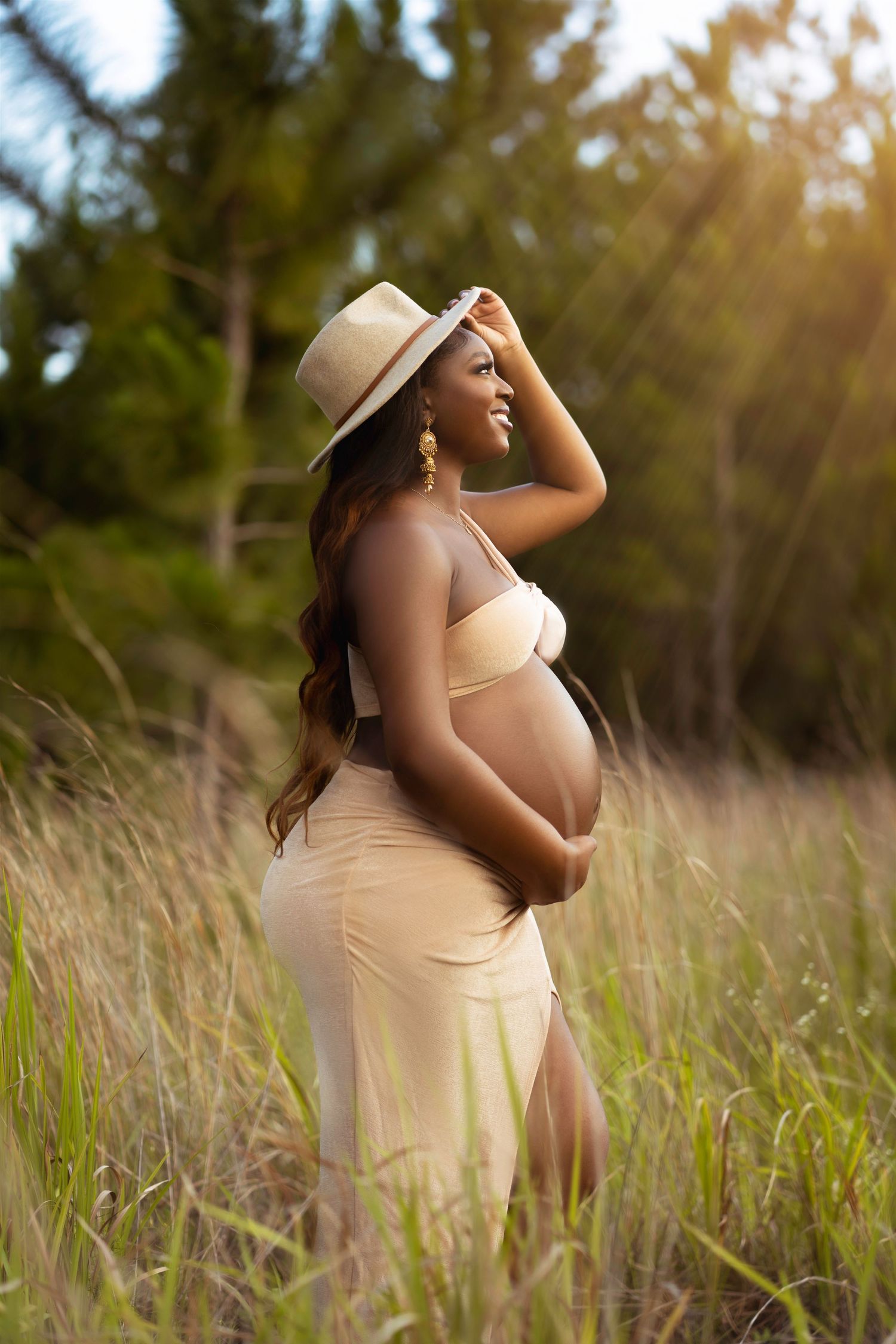 Maternity photoshoot in a sunlit meadow with tall grass during golden hour.