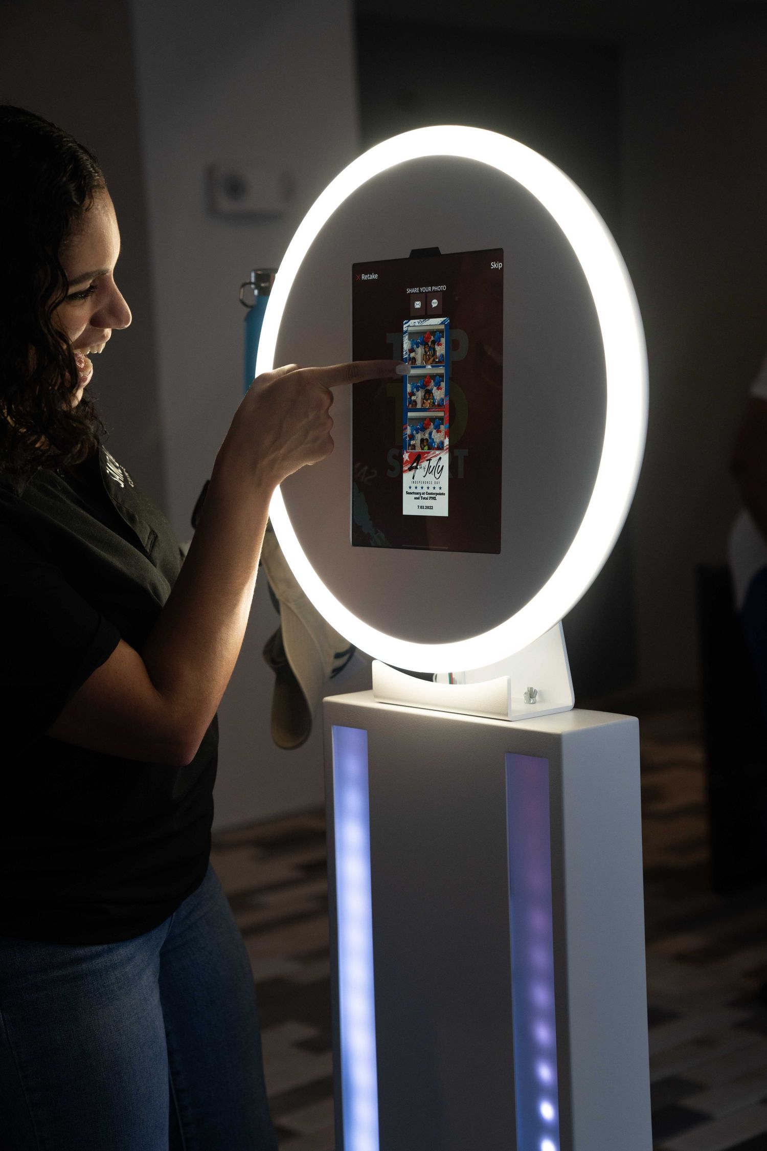 A person interacts with a large circular LED ring light mounted on a white pedestal in a dark room.