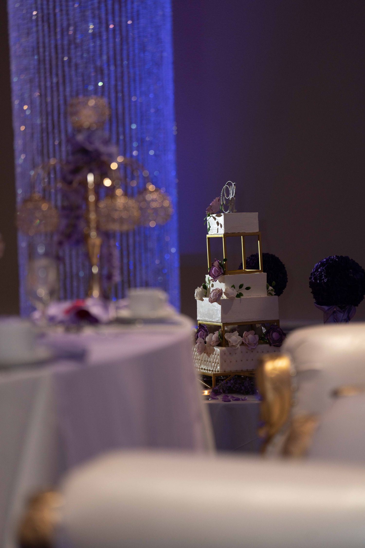 Wedding cake with cascading blue lighting and sparkly backdrop creates an elegant reception atmosphere.