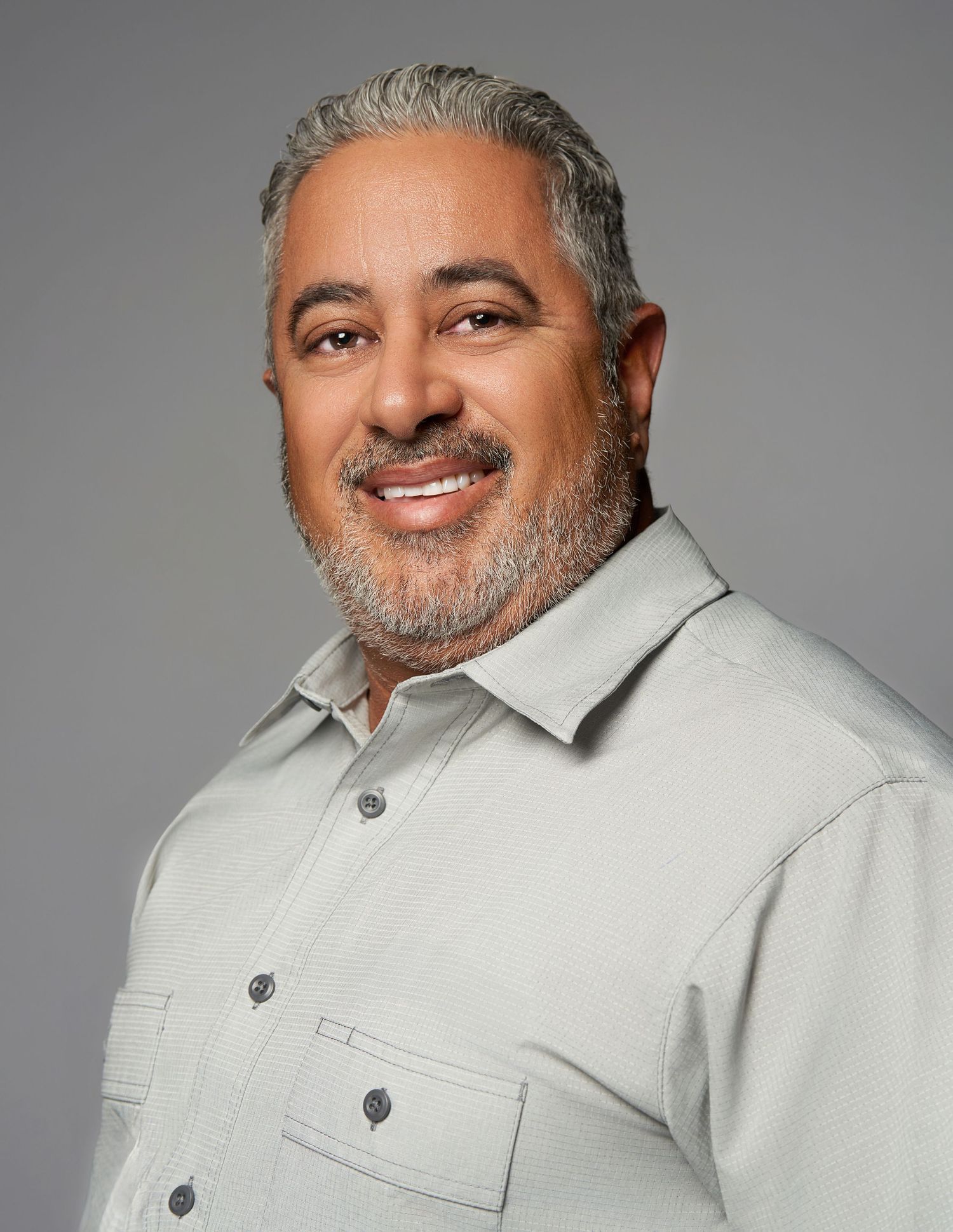 Studio portraits of a man with gray hair wearing a light colored button-up shirt.