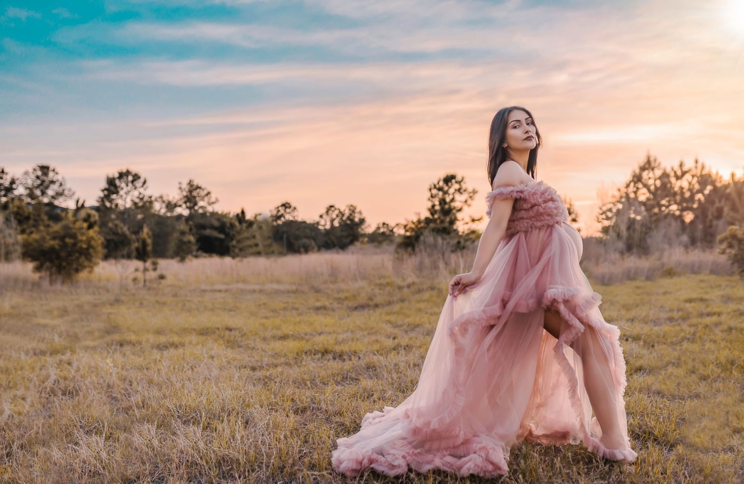 A flowing pink gown billows in the wind across a golden meadow at sunset.