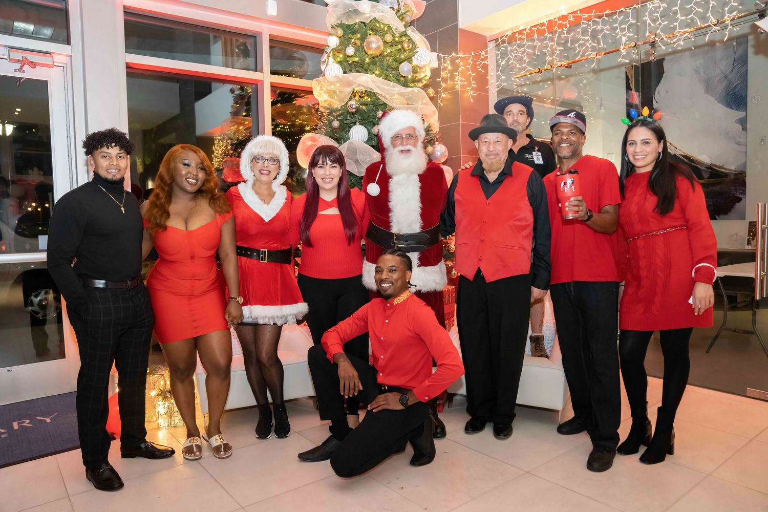 A group of performers in red and black outfits pose together at a holiday event with festive decorations.
