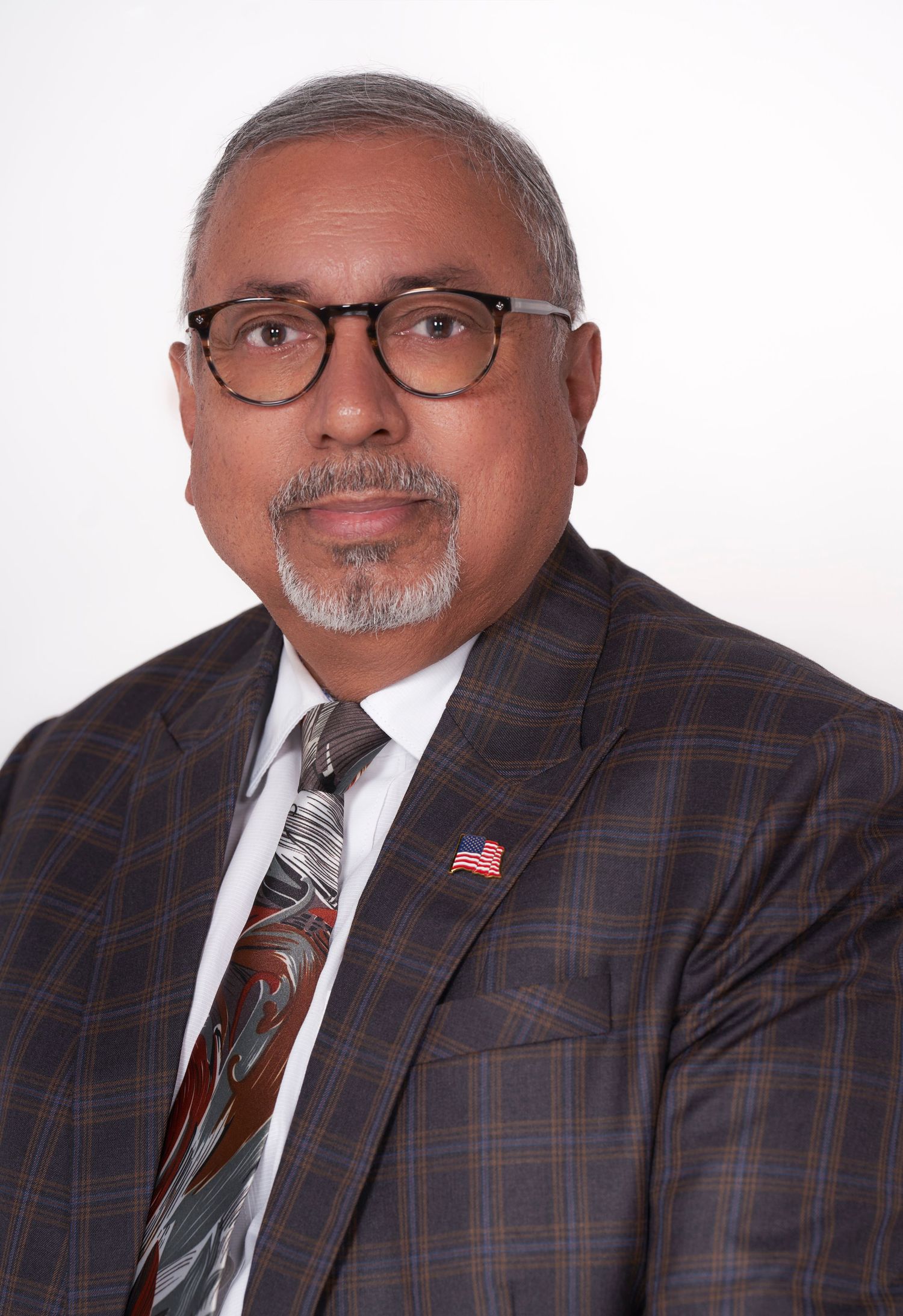 Professional portraits of someone wearing a plaid suit jacket and glasses against white background.