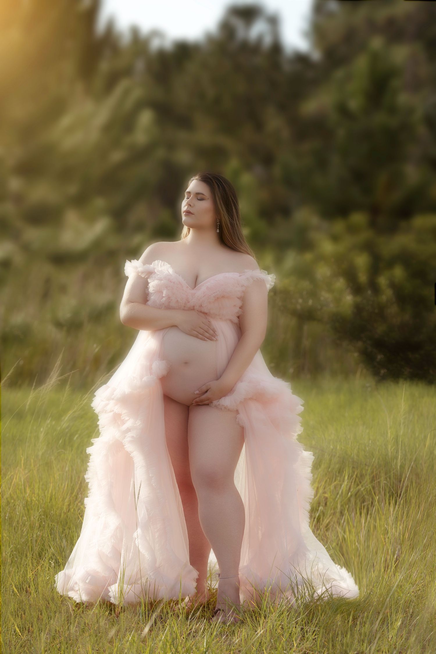 Dreamy outdoor maternity photos with person wearing pink tulle gown in a grassy field.