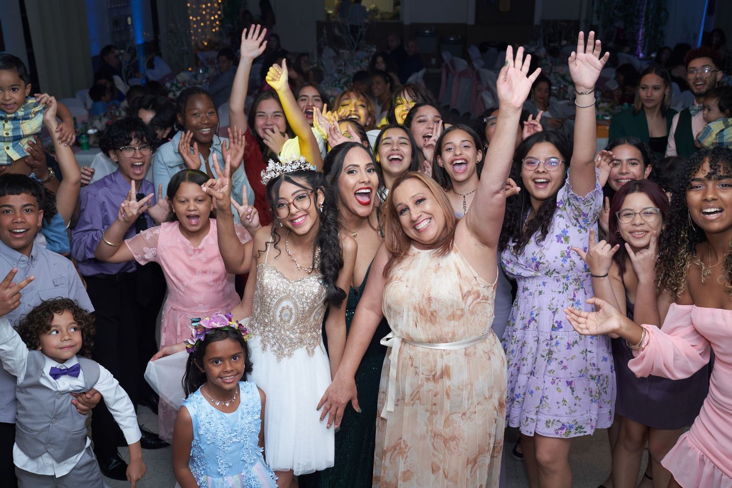 Excited party guests dancing and celebrating at a wedding reception with colorful lights in the background.