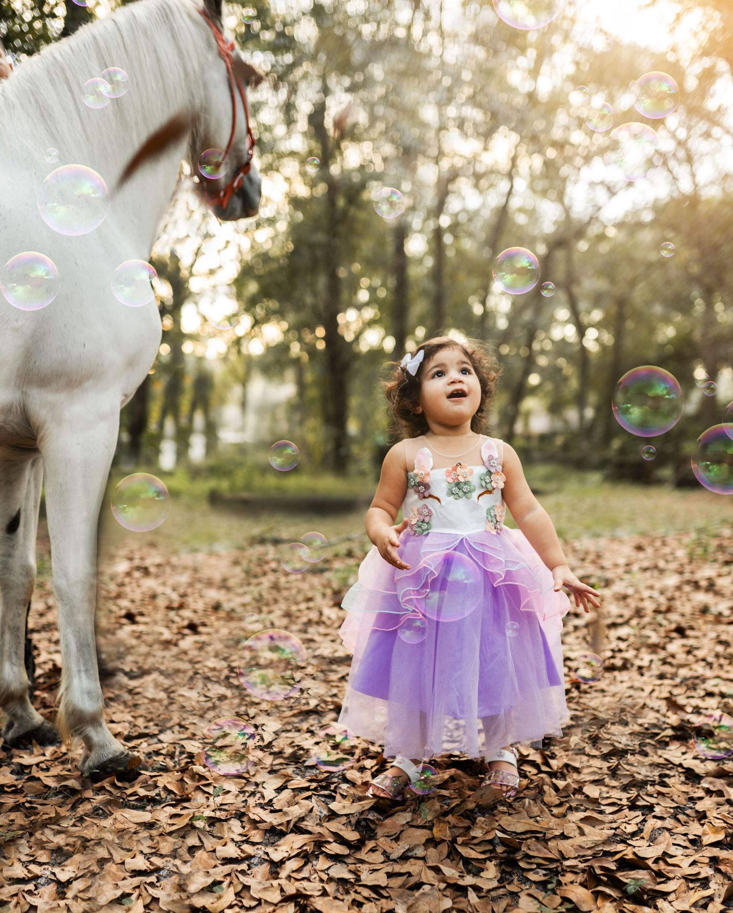 Little girl standing in front of a White horse looking up at bubbles