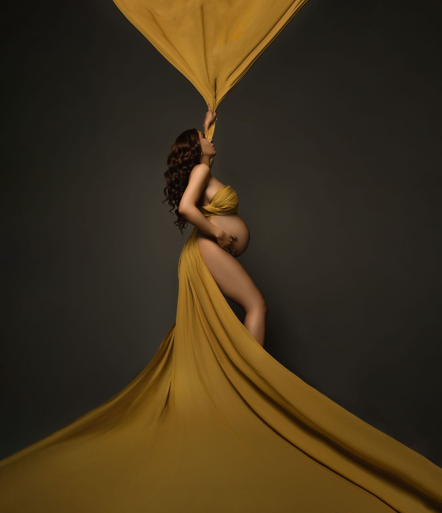 Artistic maternity photo with flowing mustard fabric against dark background.
