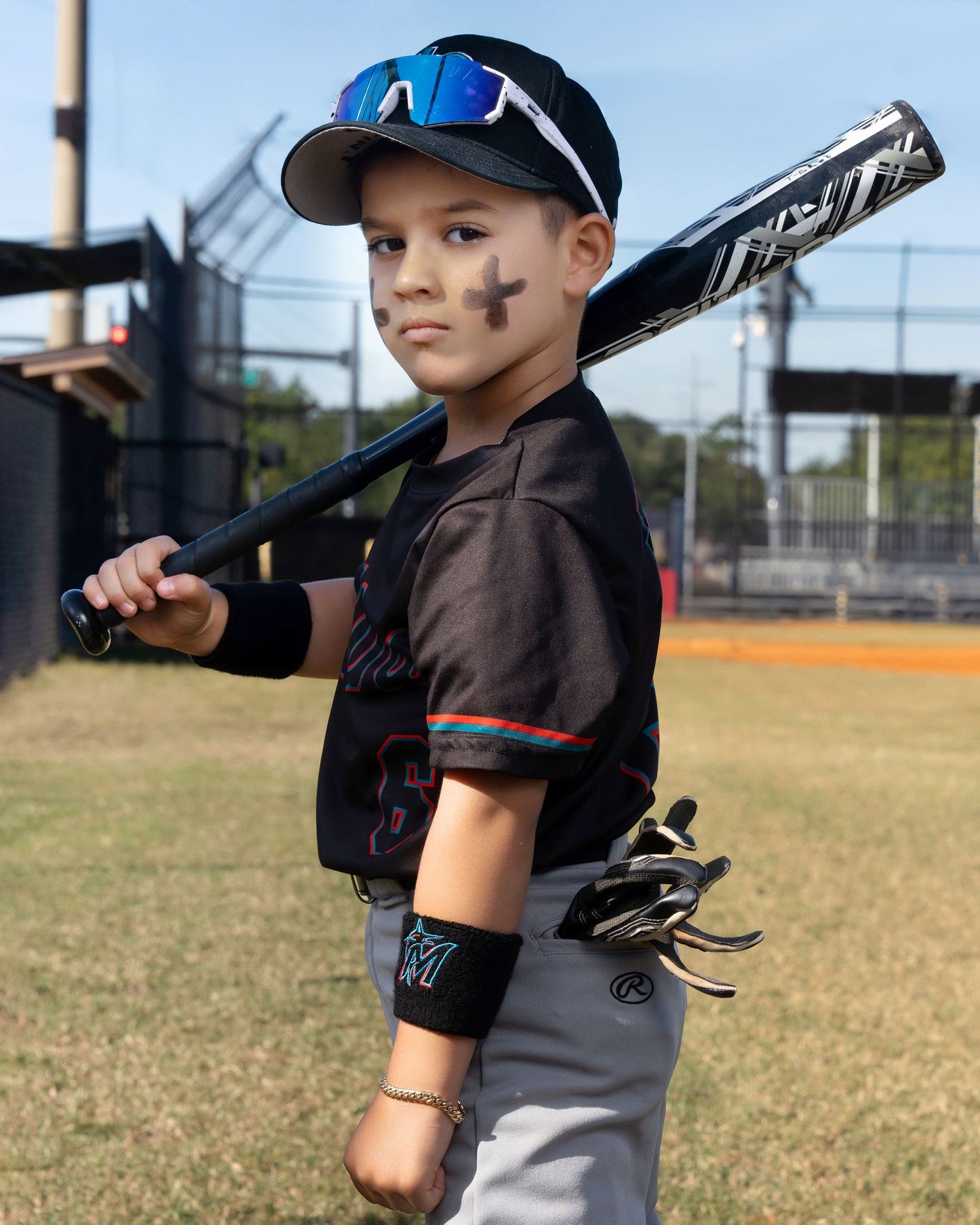 A young baseball player in a gray uniform and blue cap practices batting stance on a sunny field.