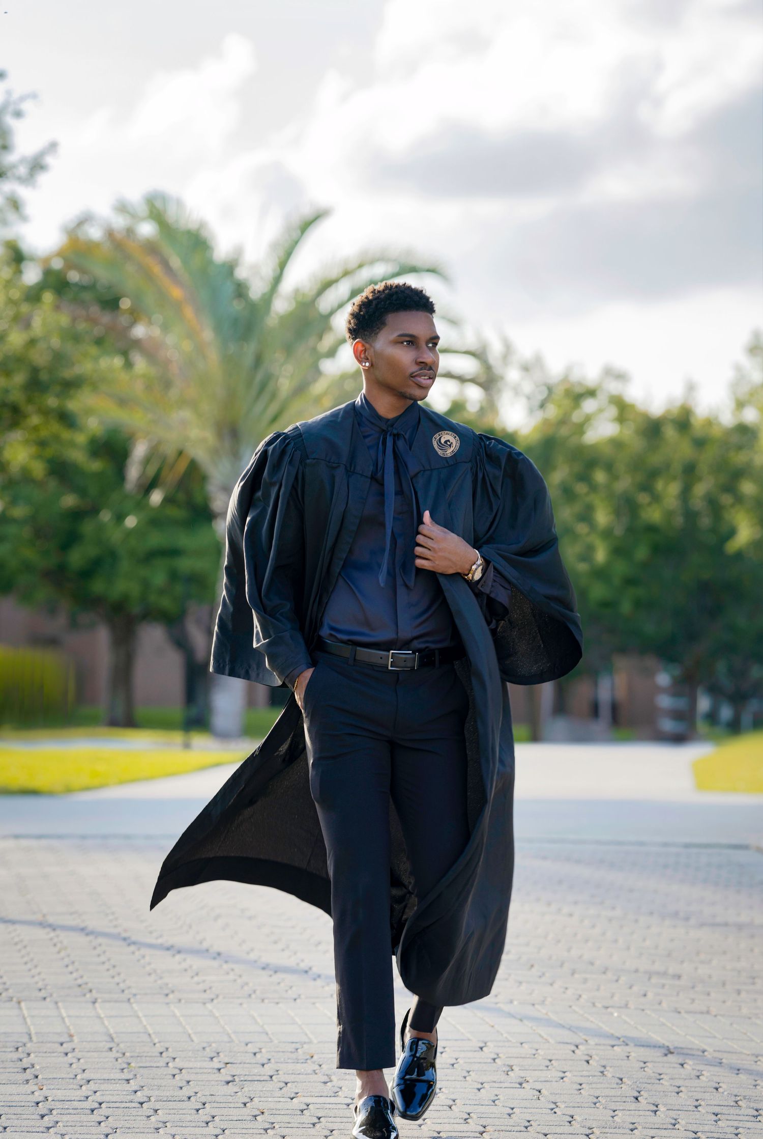 Graduate in dark blue cap and gown walking outdoors during graduation photoshoot.