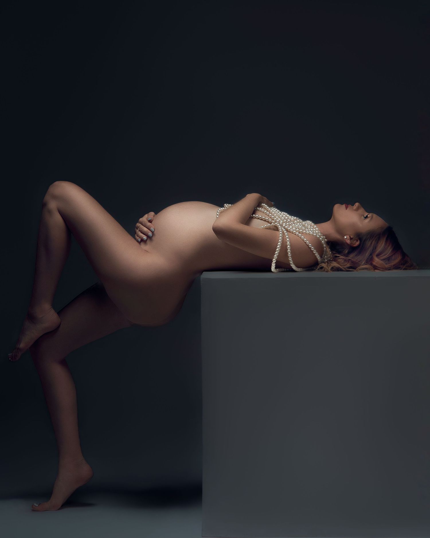 Artistic low-key maternity boudoir photography with dramatic lighting.
