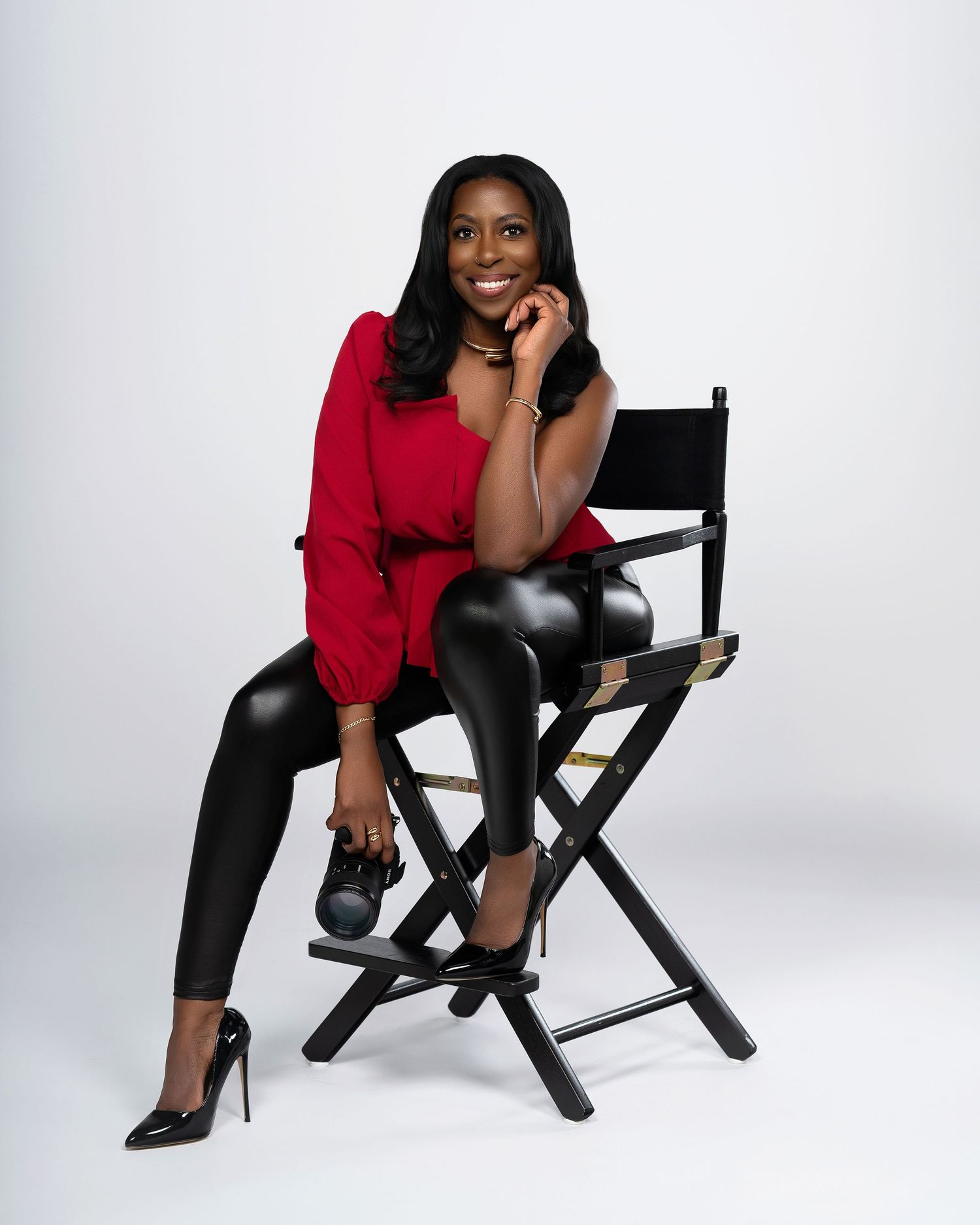 Professional studio portrait of the business owner in a red top and leather pants seated on a director's chair.