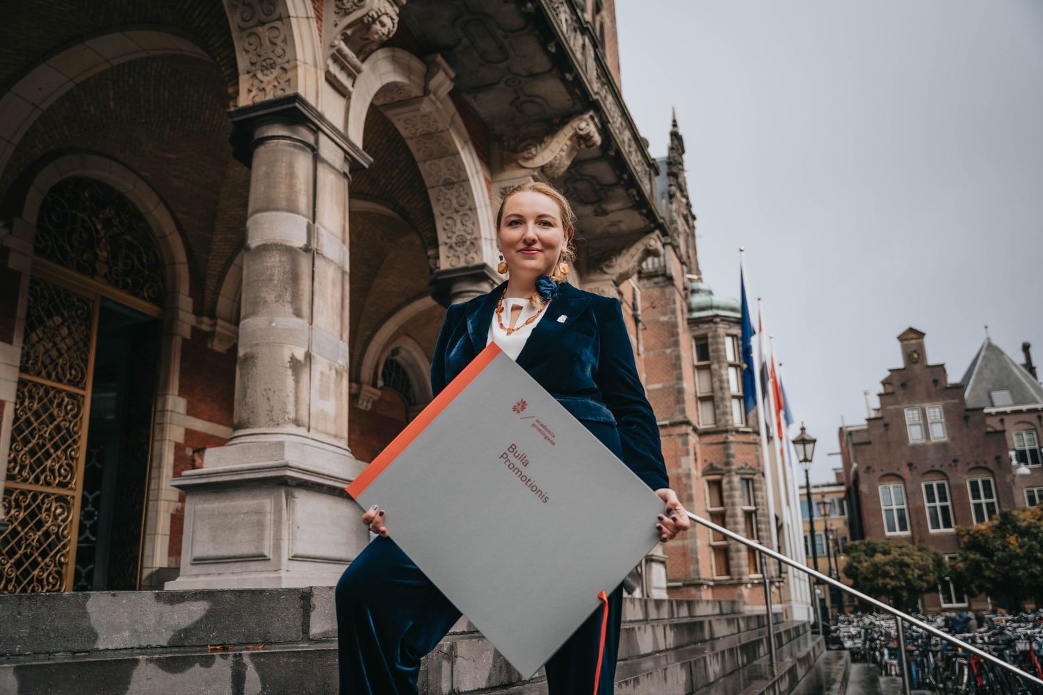PhD candidate on the stairs outside with diploma