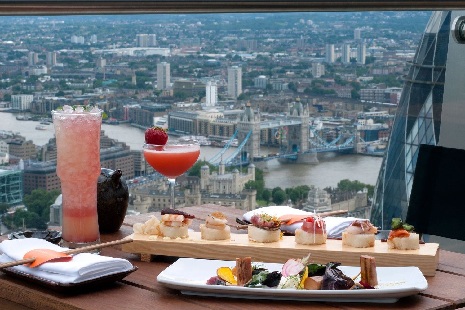 Luxury afternoon tea with cocktails overlooking Tower Bridge from The Shard, London, featuring elegant finger sandwiches and pastries.
