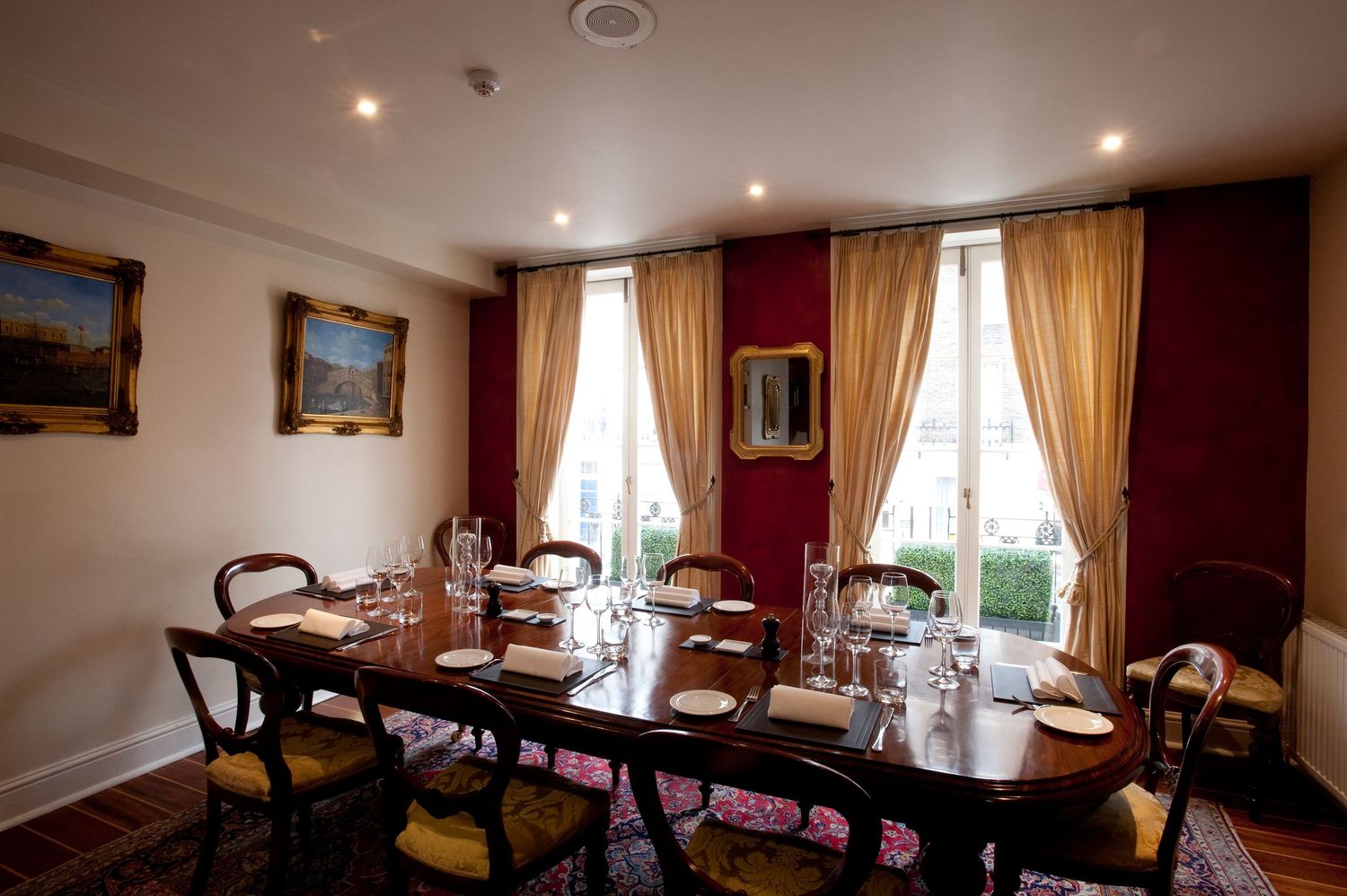 Elegant private dining room with long wooden table, gold curtains, red walls, and classic chairs set for a formal dinner.