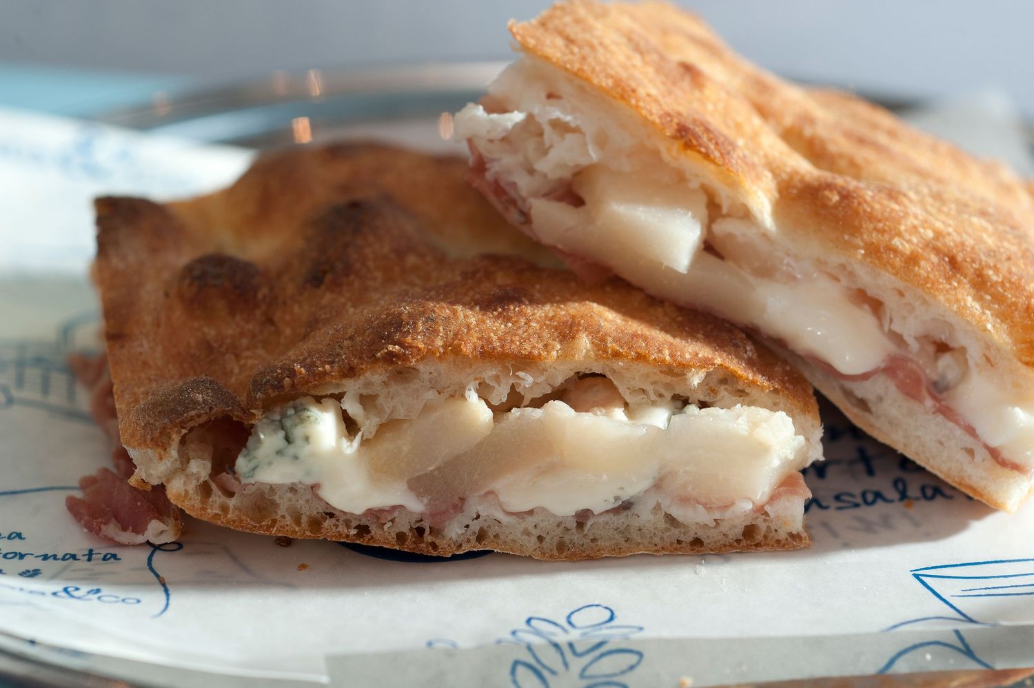 Close-up of a toasted panini sandwich filled with melted cheese, cream cheese, and ham on a white plate.