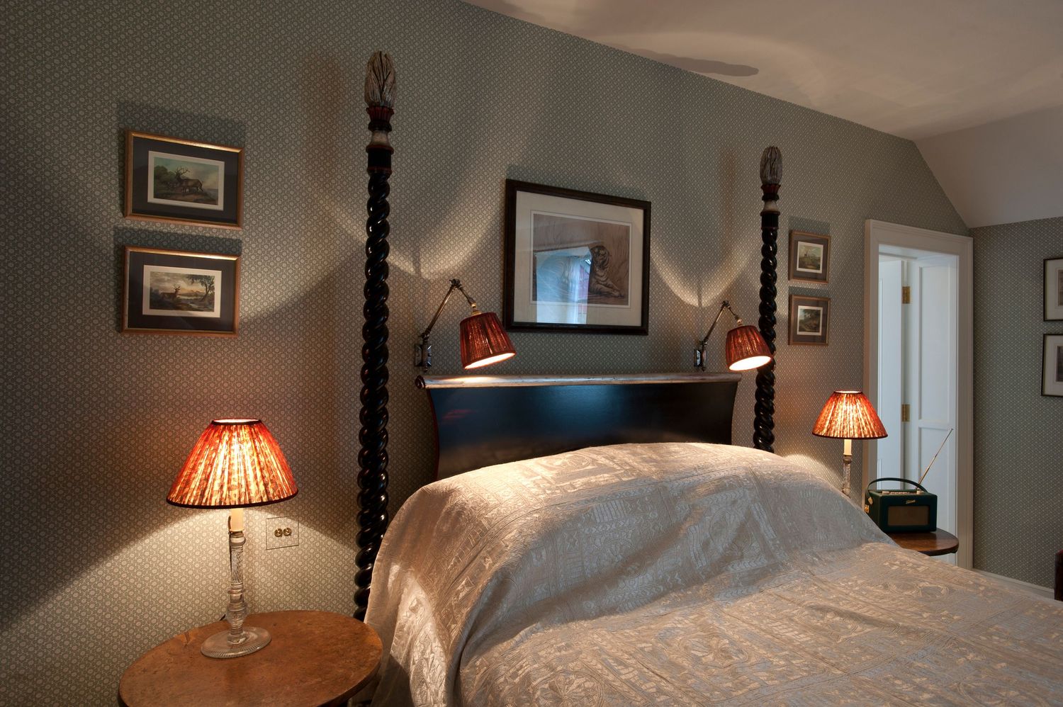 Elegant four-poster bed with white linens, warm bedside lamps, and framed artwork in a cozy bedroom.