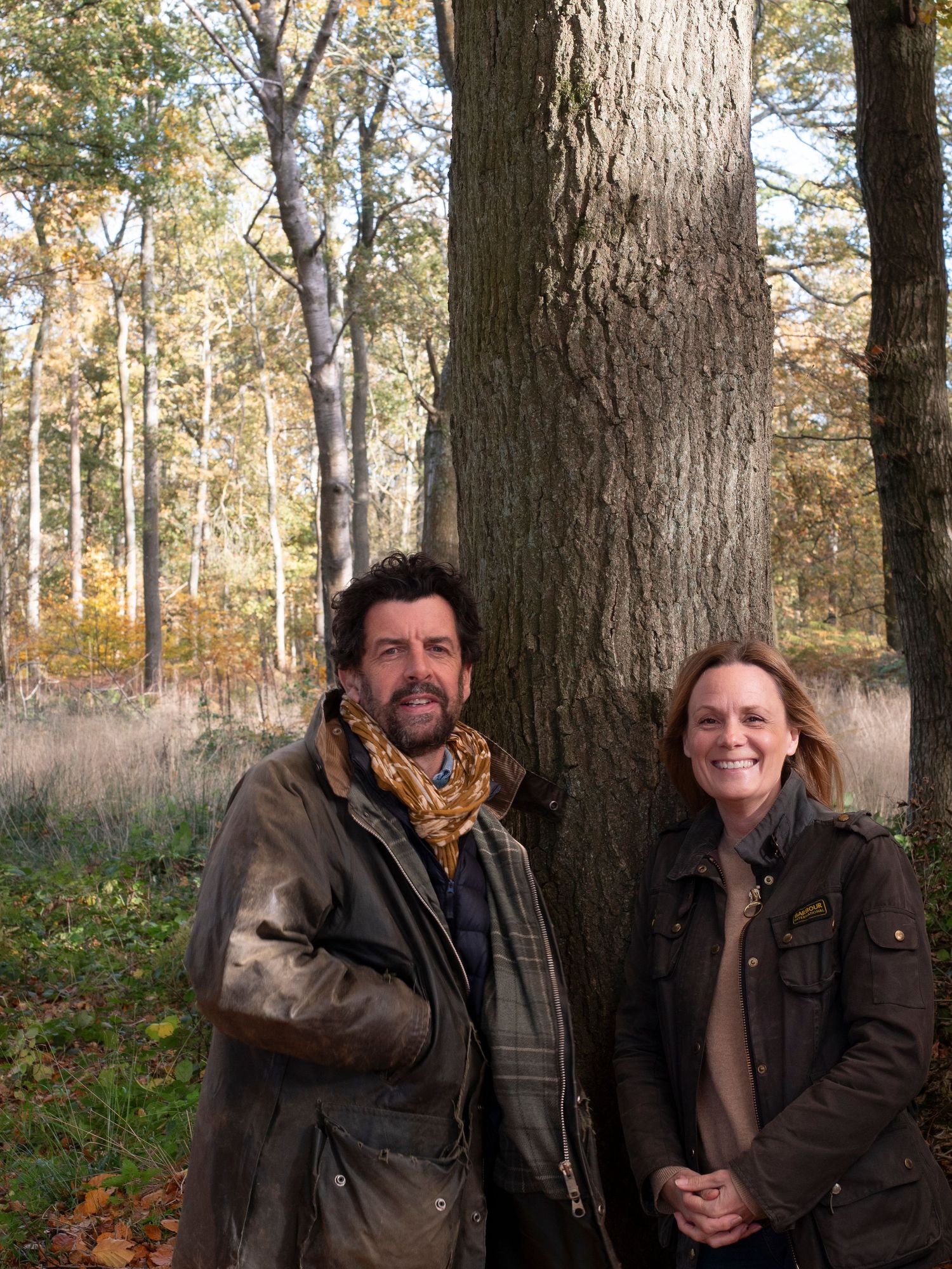 Ross and Michelle for family photograph for 'Before they Fly the Nest (husband and wife) standing beside large tree trunk in autumn forest.