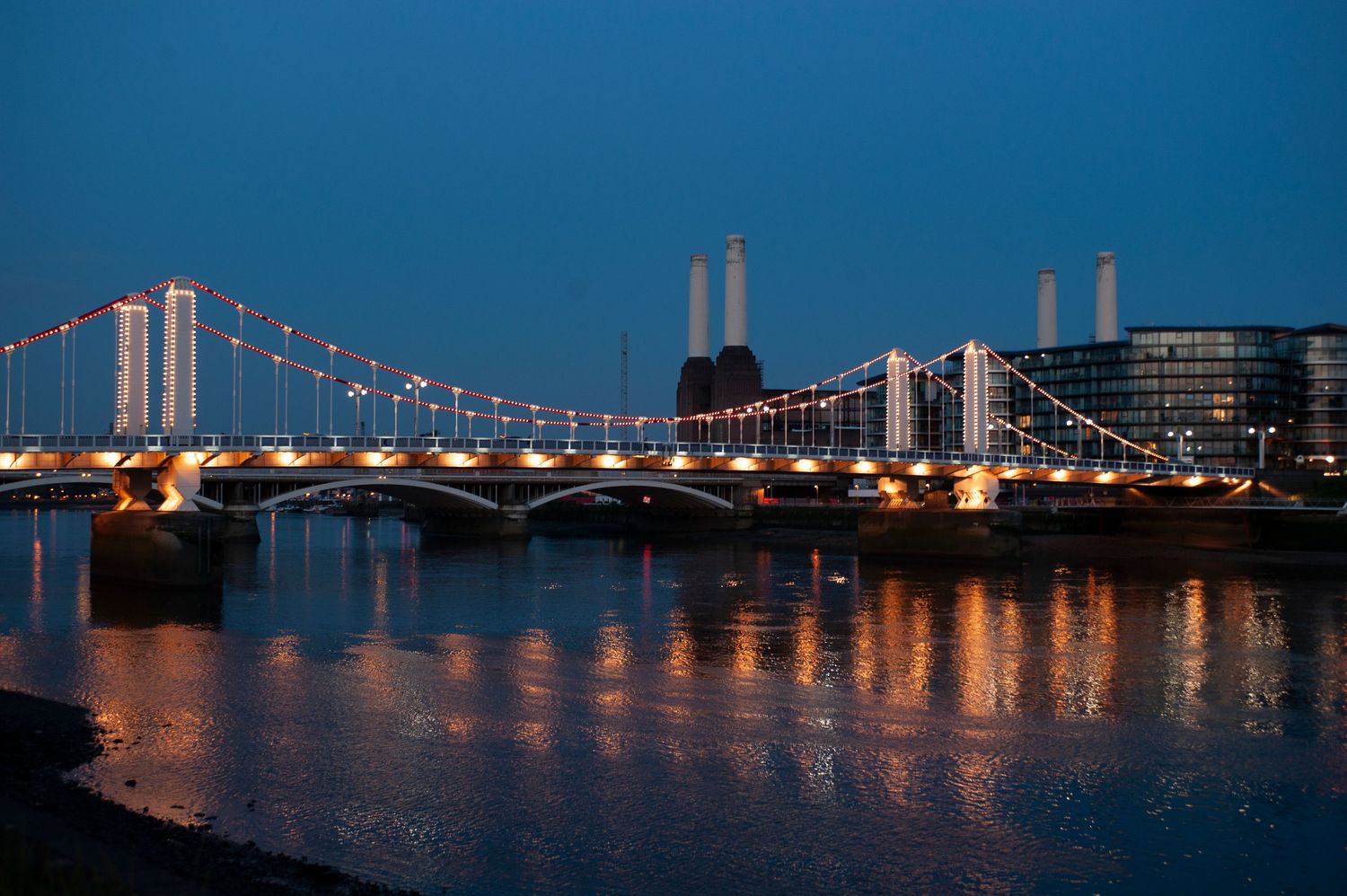 Dusk view of Battersea Power Station chimneys silhouetted against dark blue sky with Chelsea Bridge in foreground.
Photograph by Danny Elwes