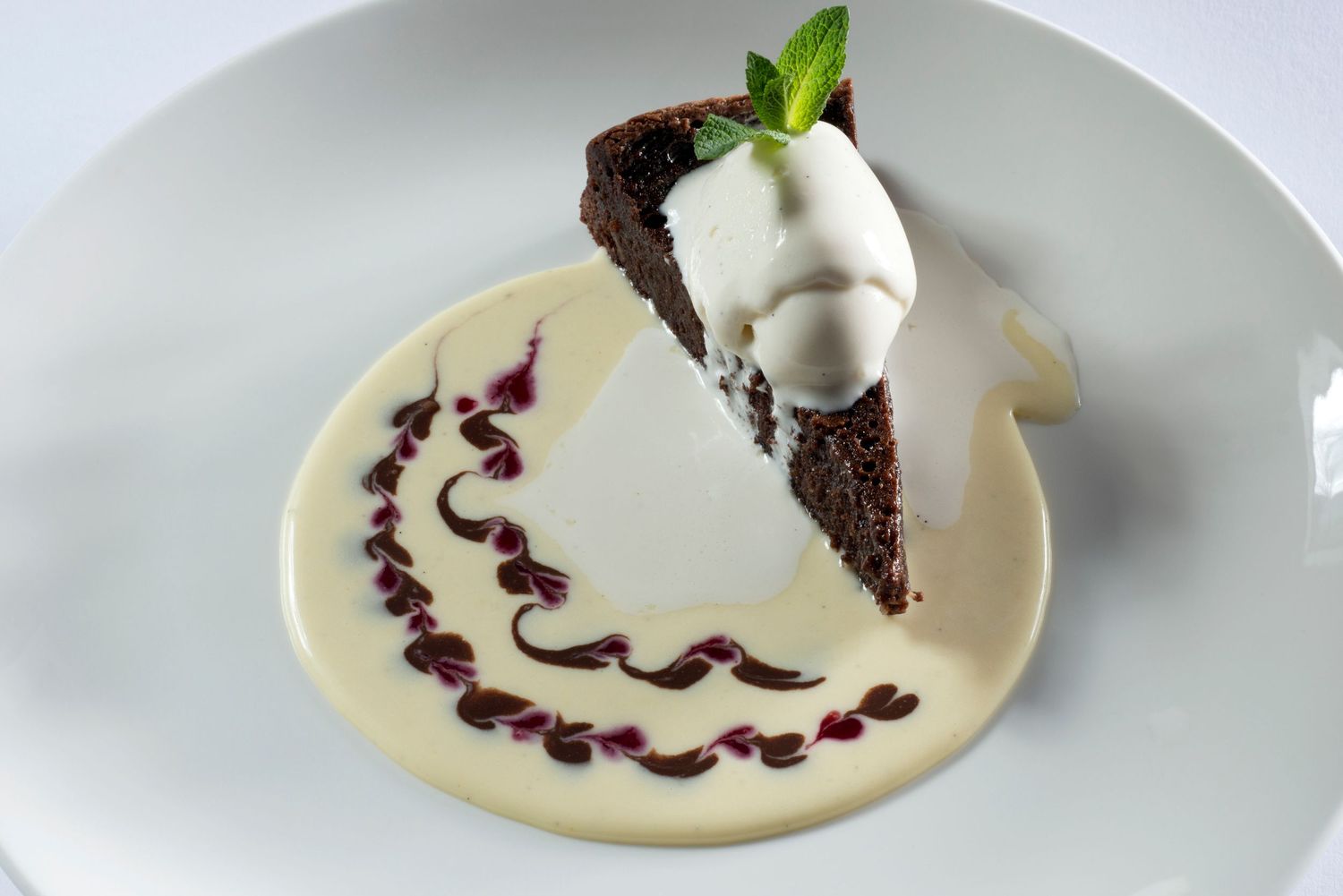 A decadent chocolate cake slice topped with whipped cream and mint, served on a white plate with vanilla sauce swirl.