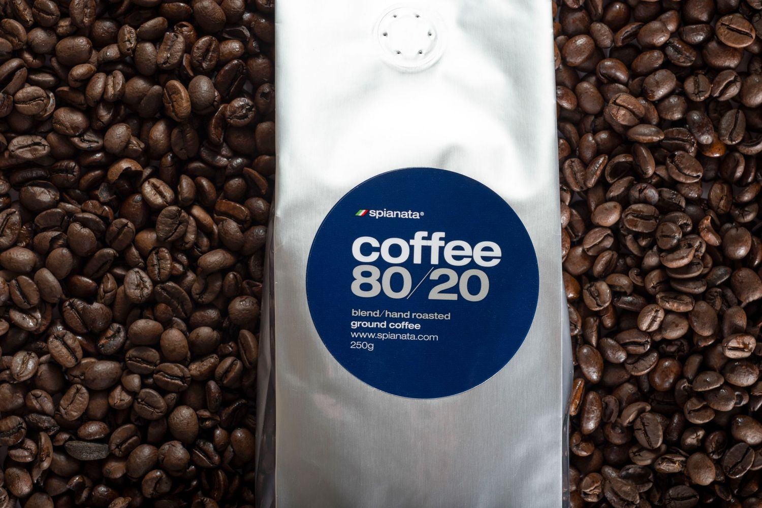 Aperada Coffee 80/20 blend silver bag of ground coffee surrounded by roasted coffee beans.