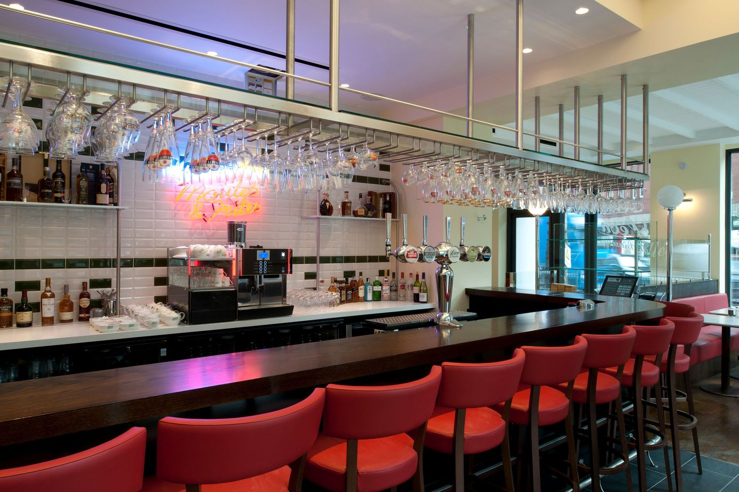 Modern bar with red stools, hanging wine glasses, and a well-stocked back bar in an elegant restaurant setting.