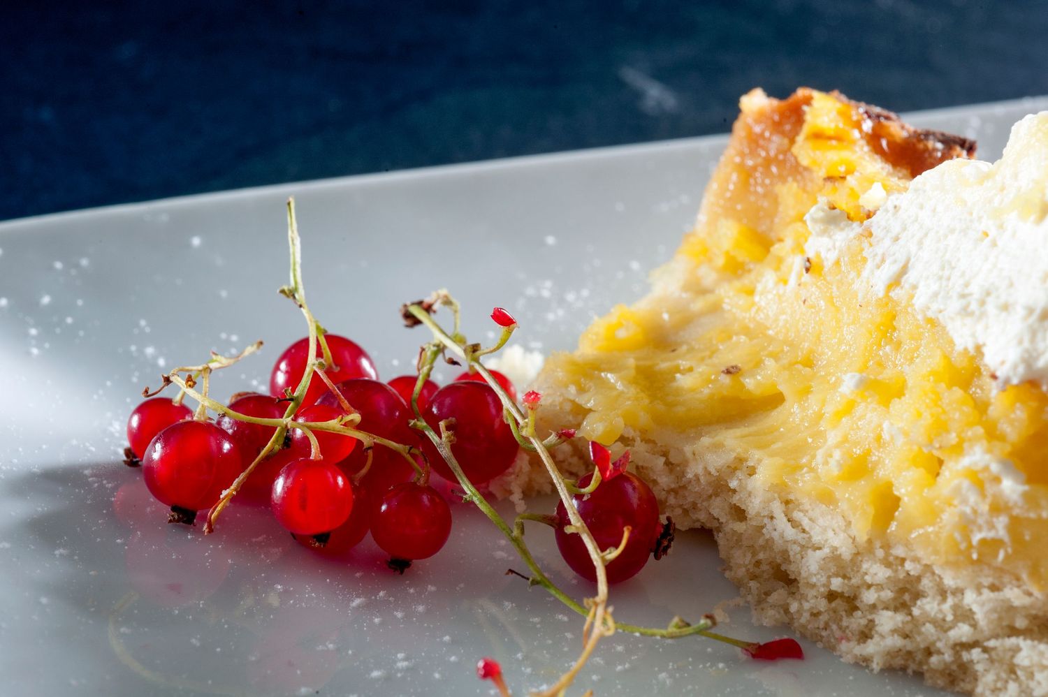 A slice of moist yellow cake dusted with powdered sugar, served with fresh red currants on a white plate.