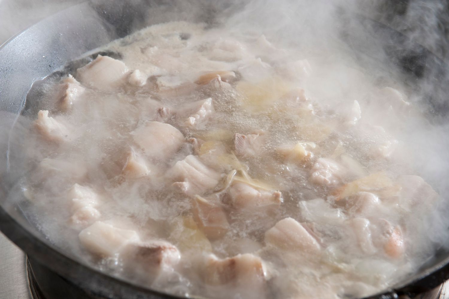 Chunks of chicken simmering in a steaming hot pot of broth, creating a rich and flavorful homemade soup.