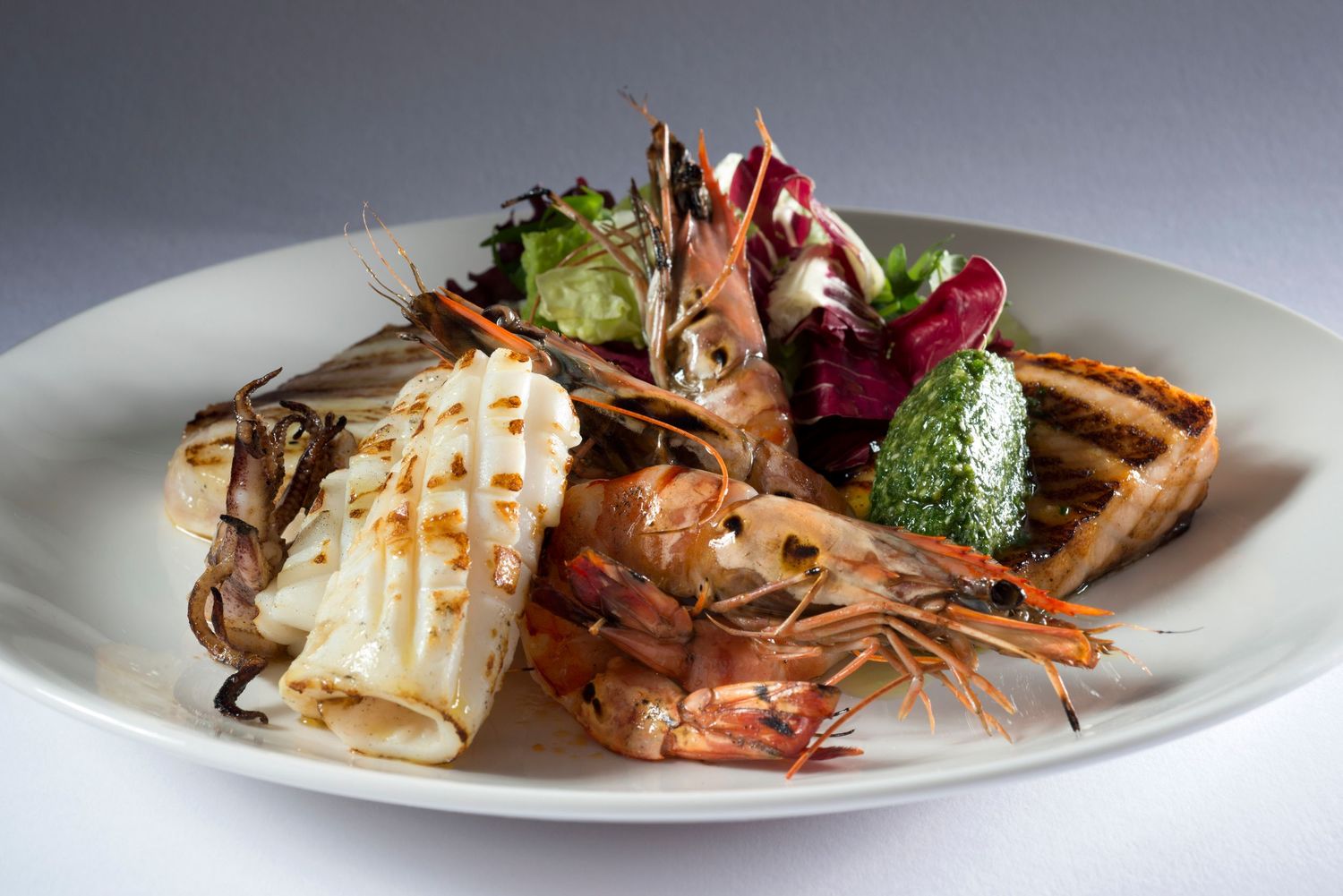 Grilled seafood platter with prawns, squid, and mixed greens on a white plate.