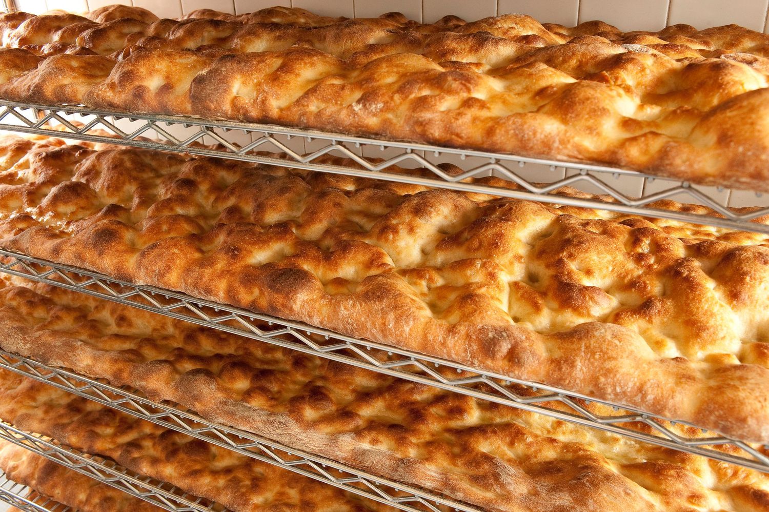 Freshly baked golden-brown flatbreads cooling on wire rack shelves in a bakery.
