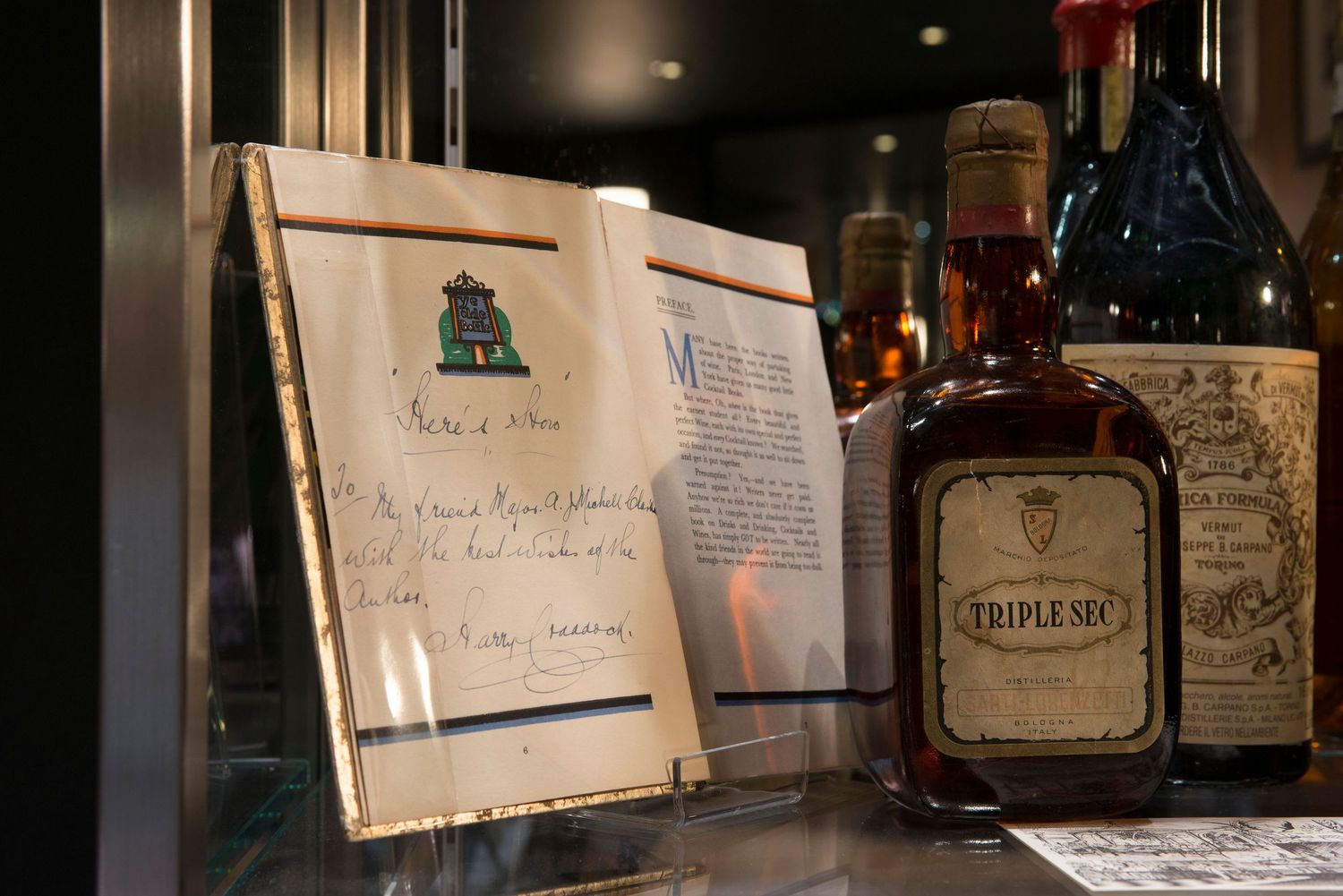 Vintage Triple Sec liqueur bottle displayed beside a framed handwritten note in a glass cabinet.