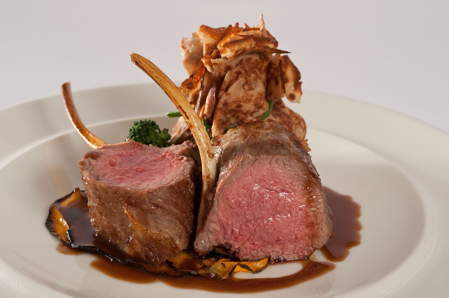 Medium rare lamb cutlets with crispy garnish and sauce on white plate.
Photograph by Danny Elwes