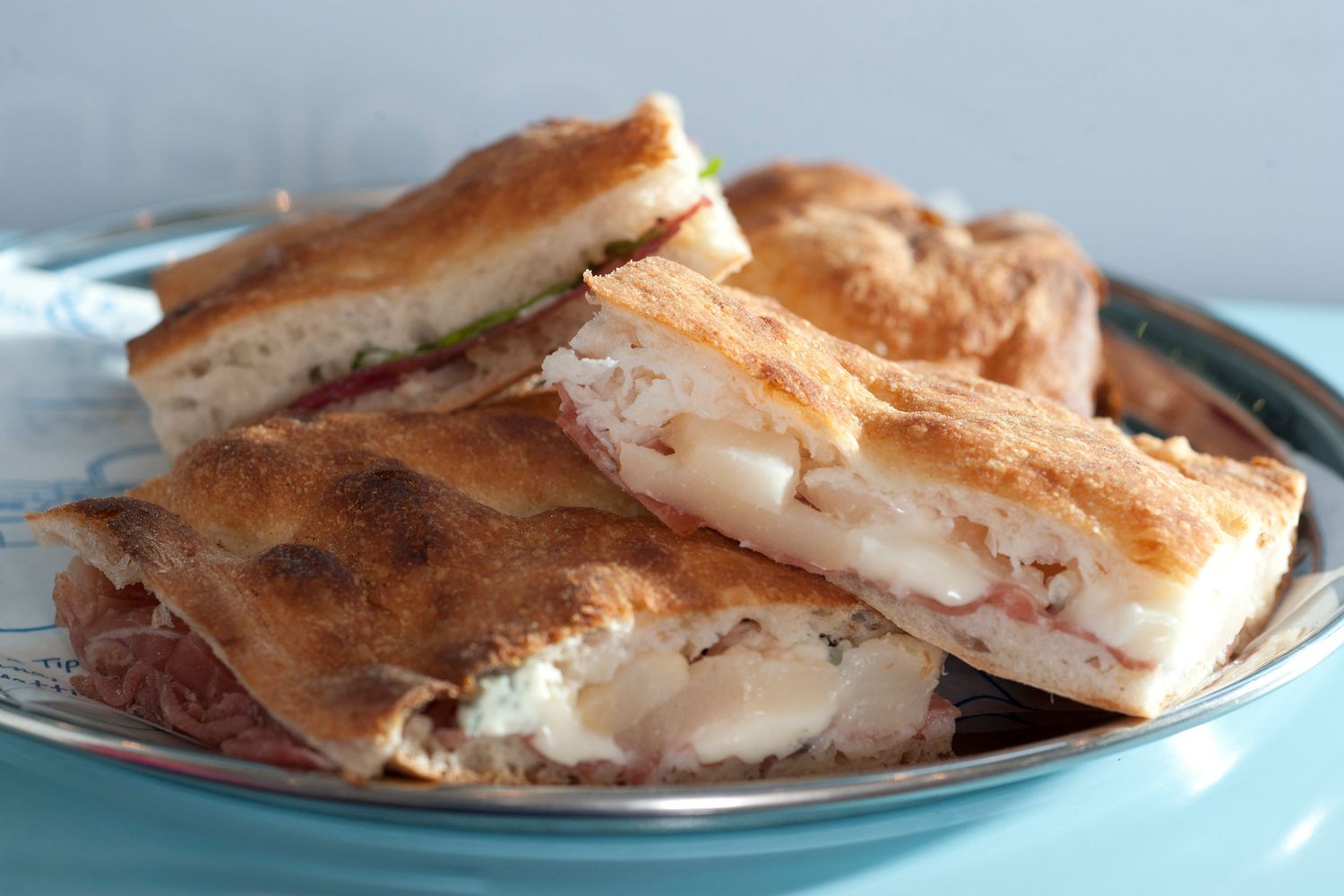 Sliced panini sandwiches with melted cheese and fresh ingredients served on a blue plate.