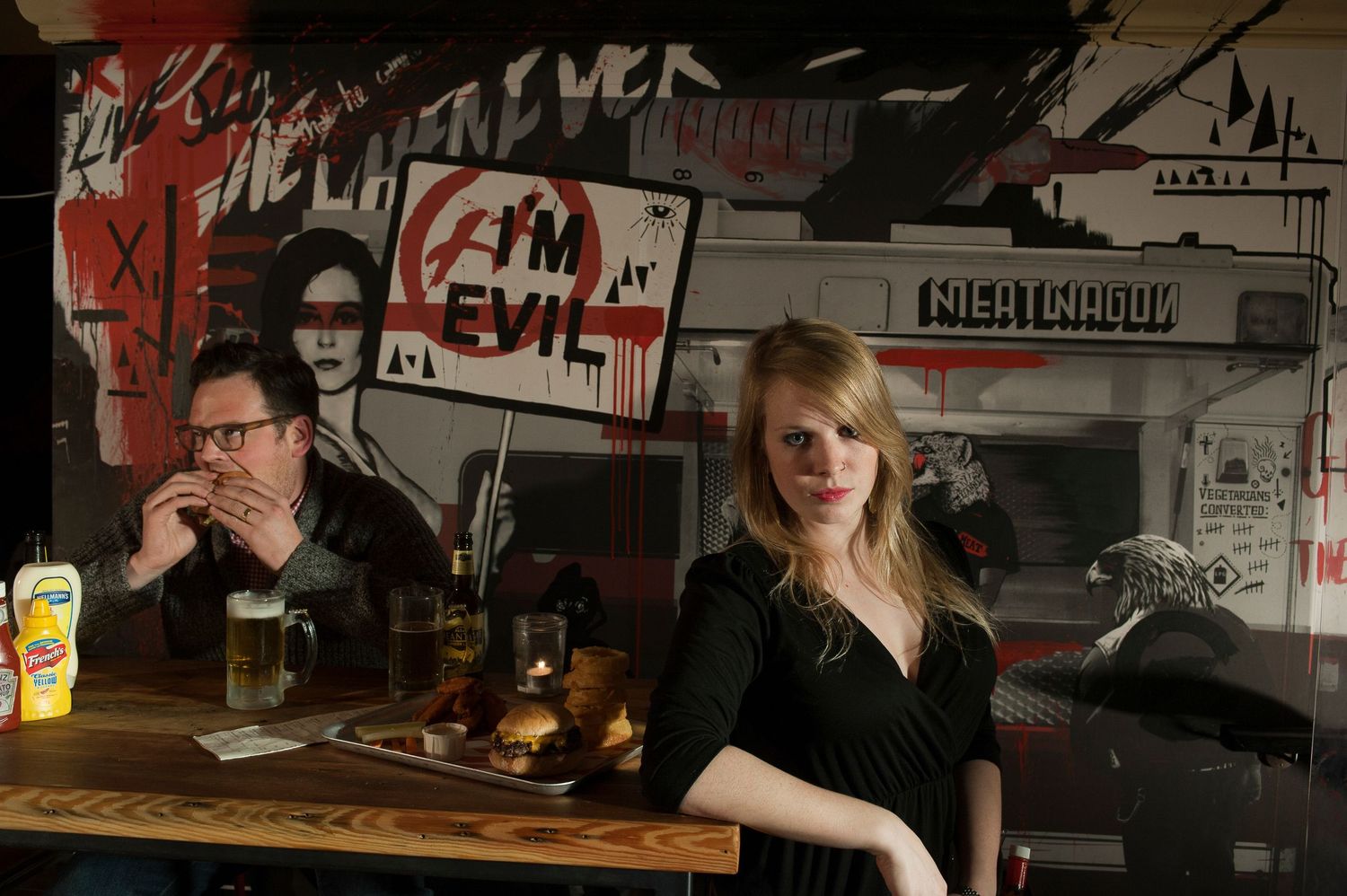 Meat Liquor burger restaurant. Chief Burgerette posing whilst customer devours burger
Photograph by Danny Elwes