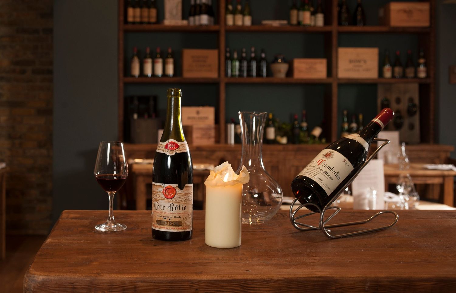 Elegant restaurant table with wine bottles, candle, and glasses, with a wine rack display shelf in the background.