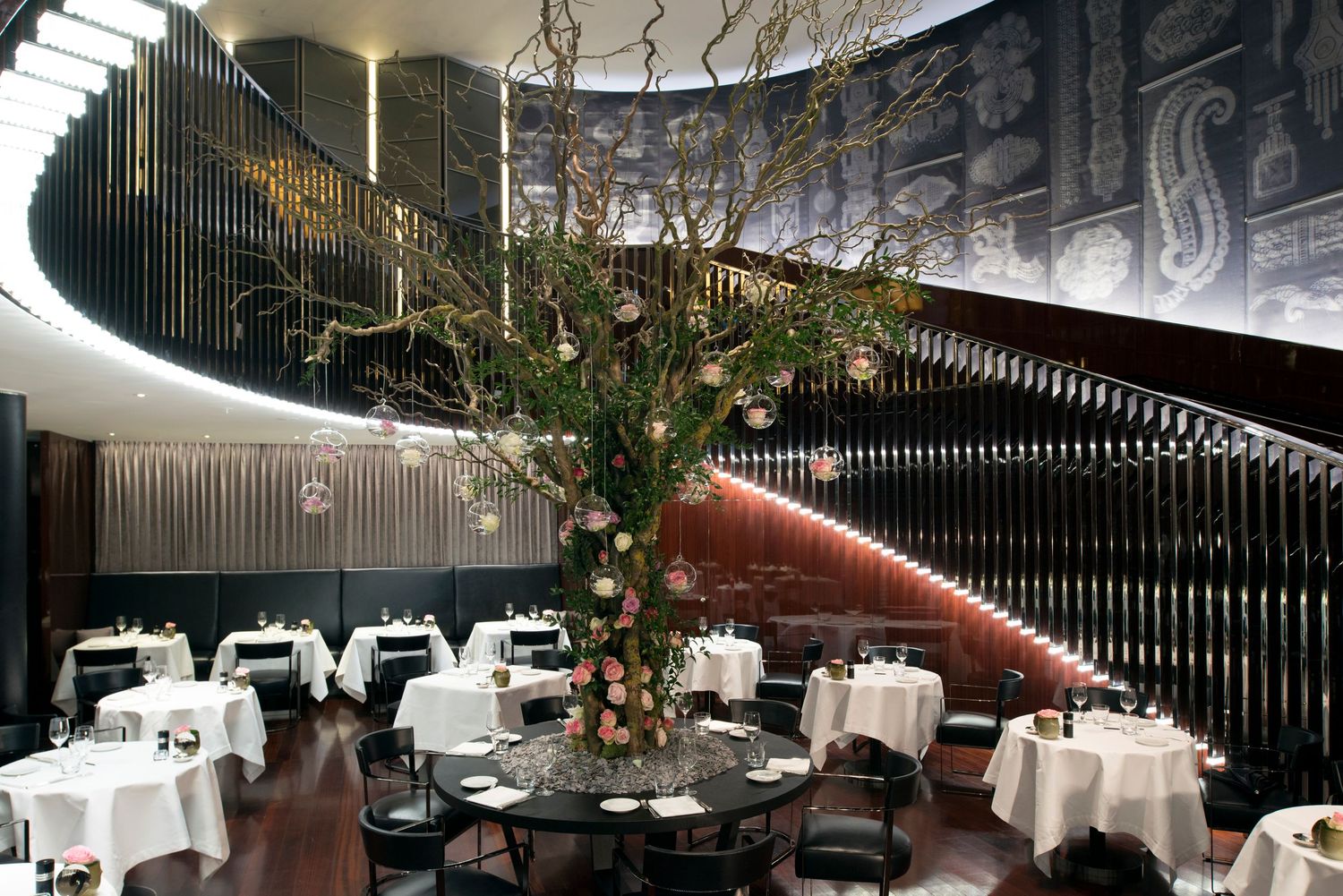 Elegant fine dining restaurant interior with spiral staircase, white tablecloths, and dramatic floral centerpiece.