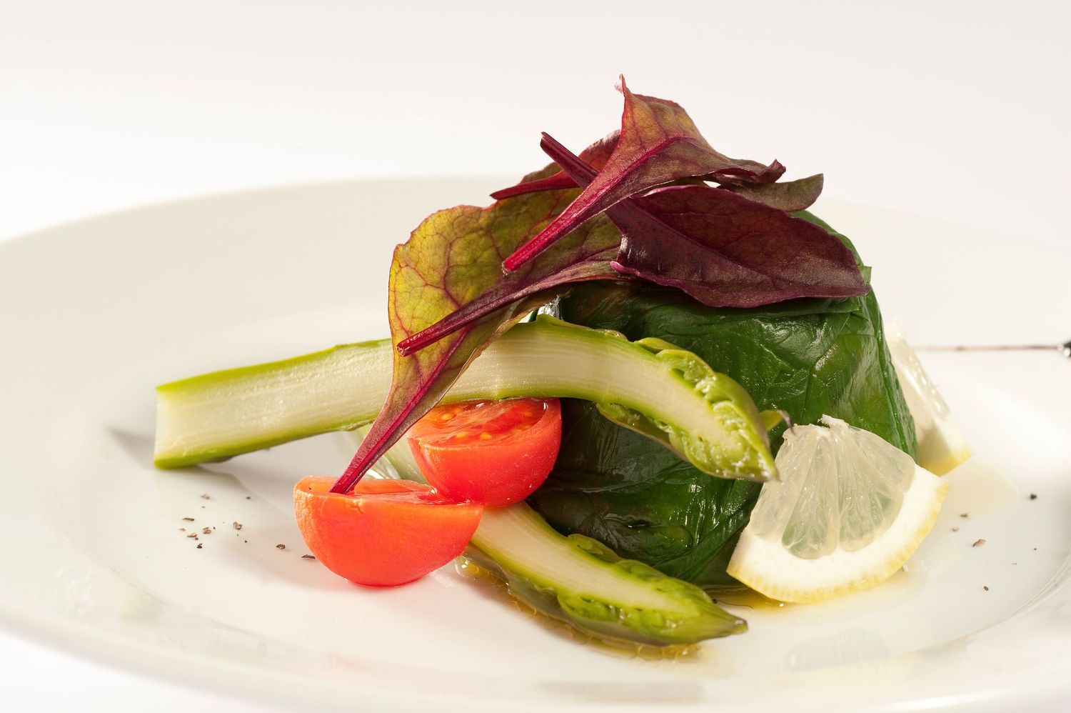 Fresh vegetable salad with cherry tomatoes, cucumber, spinach, red amaranth leaves, and lemon on a white plate.