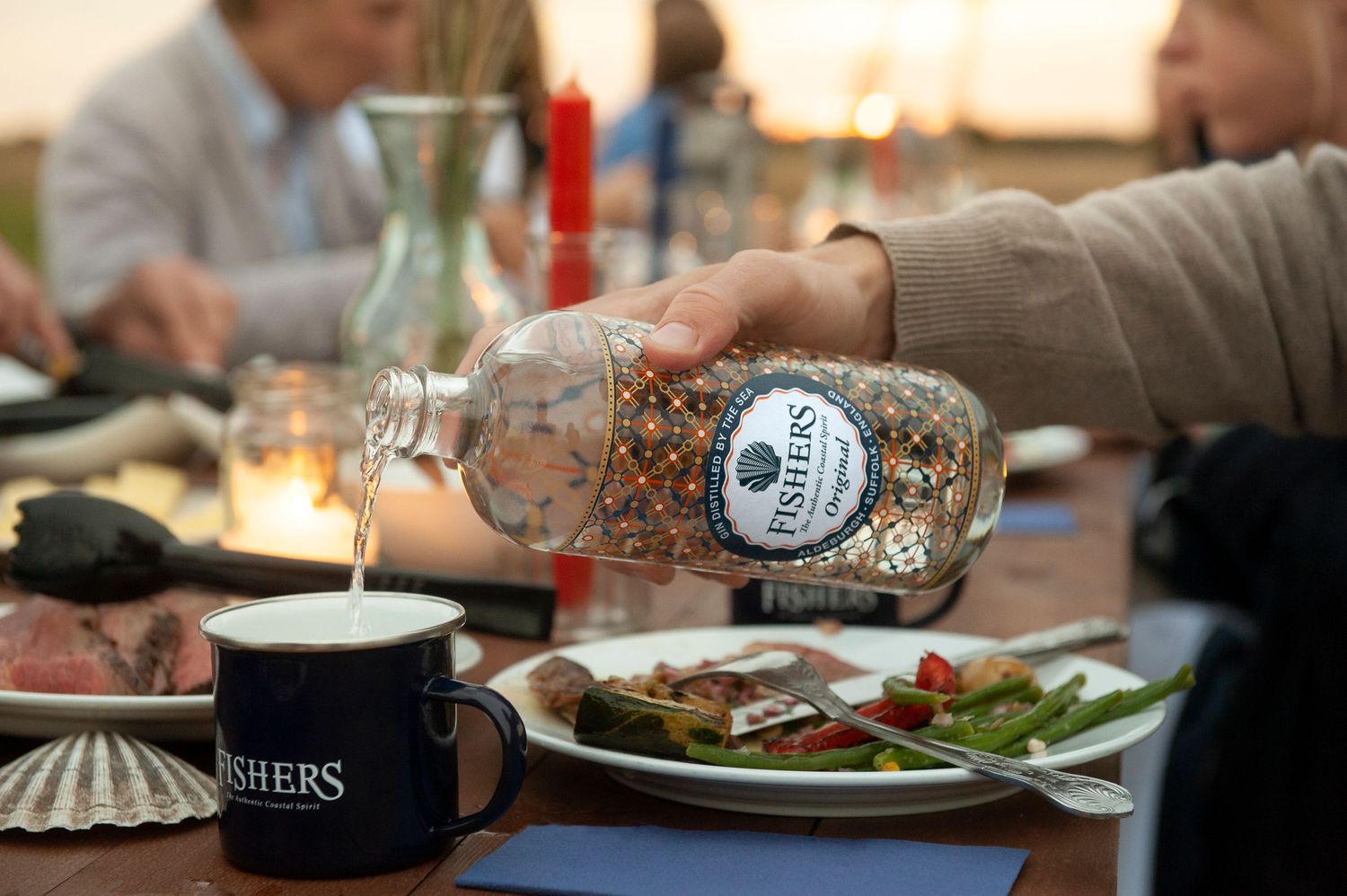 Hand pouring drink into mug at dining table with food plates. Fishers Gin shoot Suffolk coast
Photograph by Danny Elwes