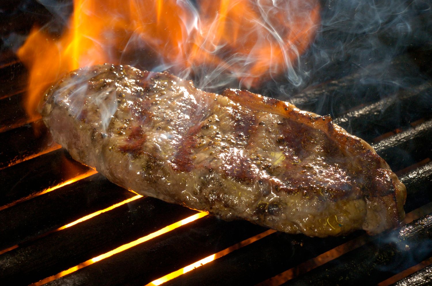Juicy grilled sausage cooking over open flames on a barbecue grill with smoke rising.