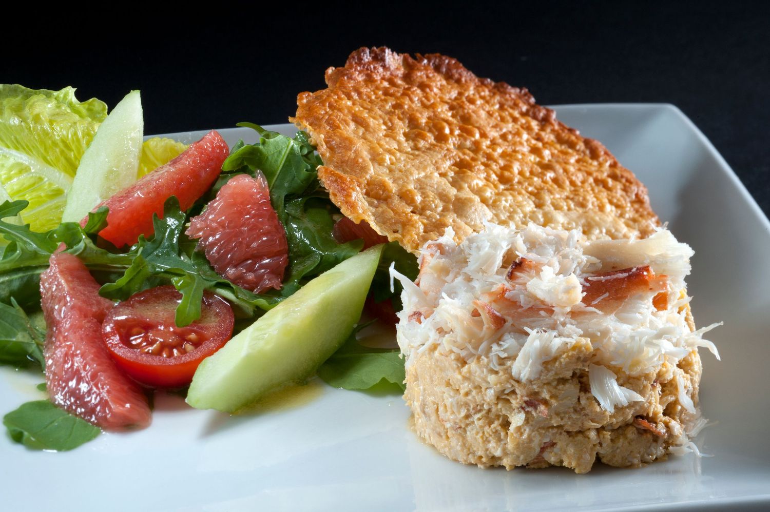 Crab salad served on toasted sesame bread with fresh greens, cucumber, tomato, and grapefruit on a white plate.