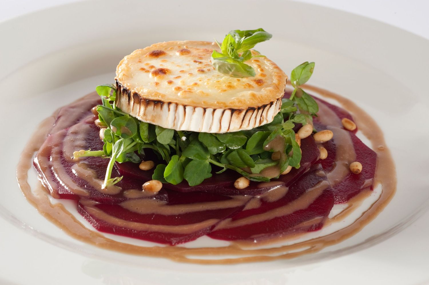 Elegant plated dish featuring grilled goat cheese on beetroot carpaccio with arugula and pine nuts in a gourmet restaurant style.