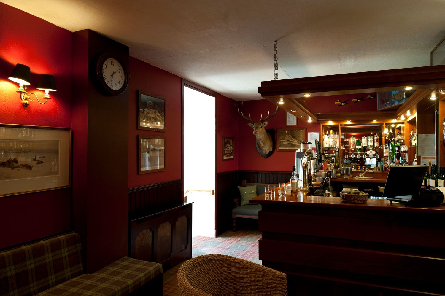 Cozy traditional British pub interior with red walls, deer head mount, vintage clock, and wooden bar counter.