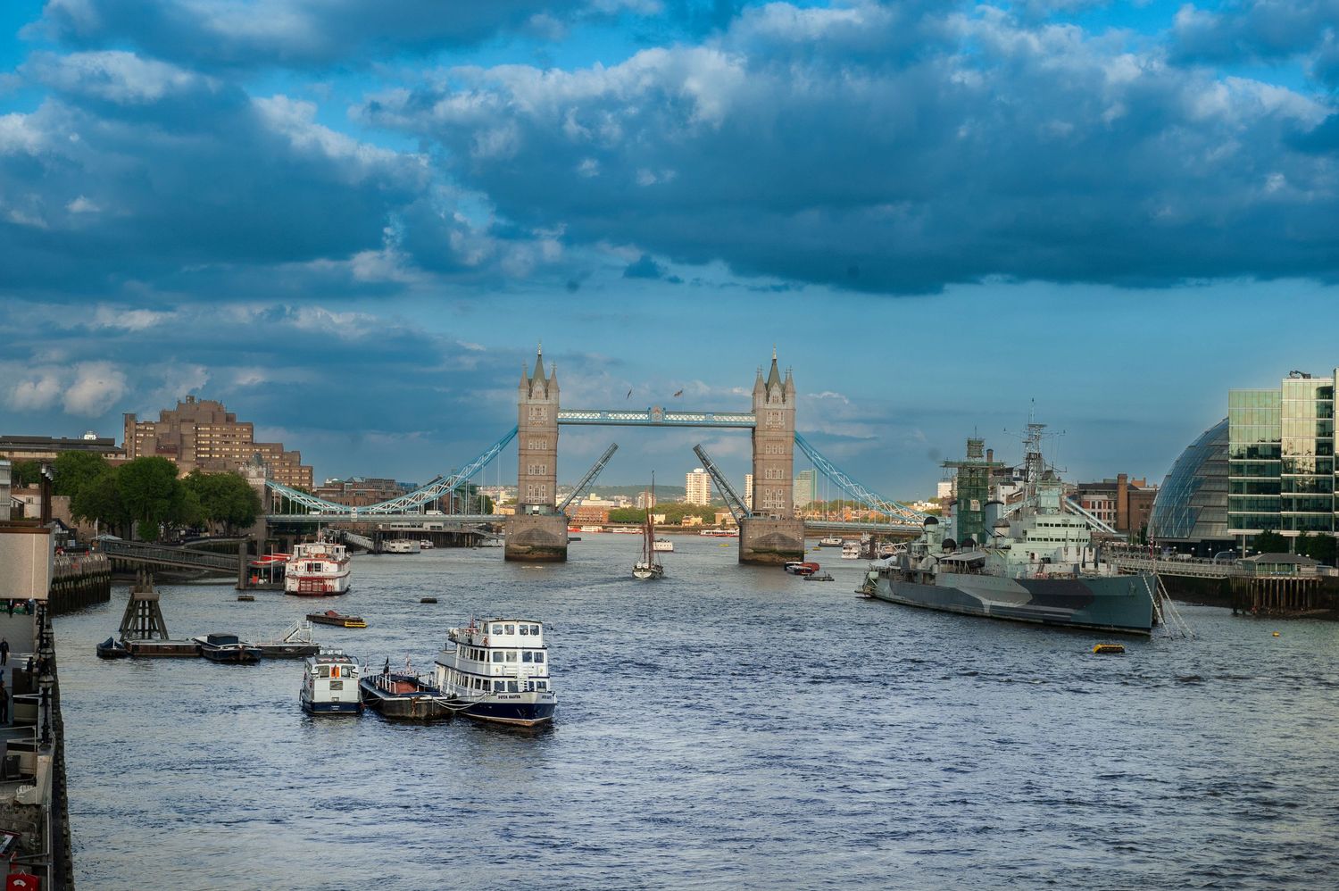 River Thames waterfront with boats and Tower Bridge under cloudy skies.
Photograph by Danny Elwes