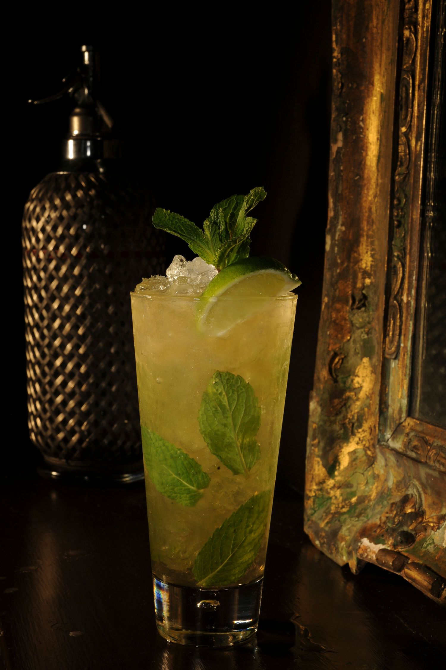 A refreshing mojito cocktail with mint leaves, lime, and ice in a tall glass on a dark bar.