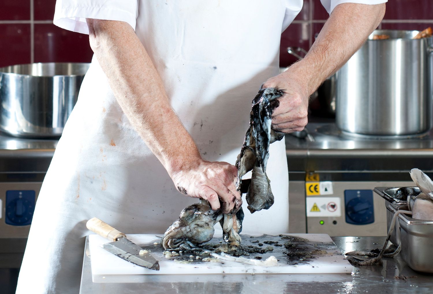 Chef preparing fresh fish on a cutting board in a professional kitchen with large stainless steel pots.
