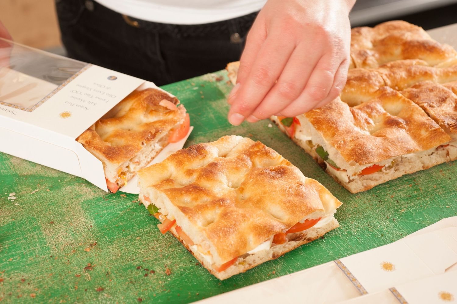 Freshly baked flatbread pizza slices on a green cutting board, with a hand reaching for a piece.