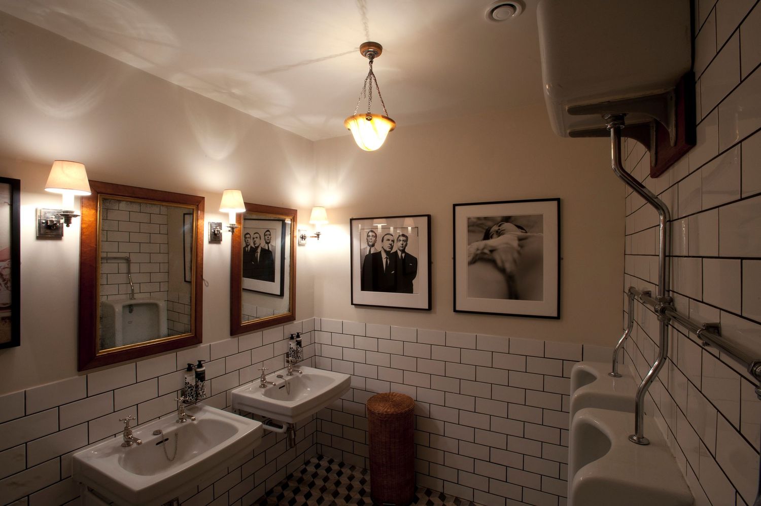Elegant vintage bathroom with white subway tiles, framed black-and-white photos, wall sconces, and classic pedestal sinks.