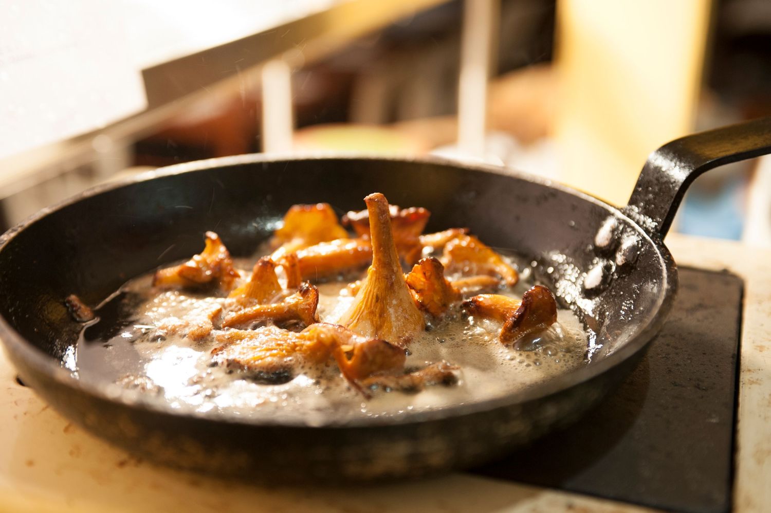 Golden chanterelle mushrooms sautéing in butter in a black cast iron skillet on a stovetop.