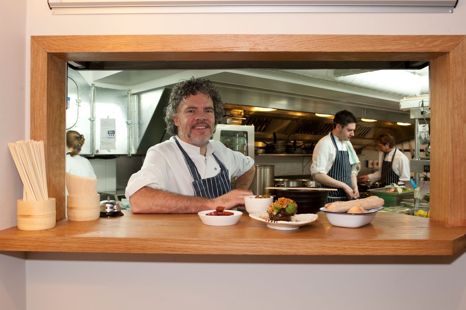View through a restaurant service window showing kitchen and dining room areas. Chef Peter Gordon
Photograph by Danny Elwes